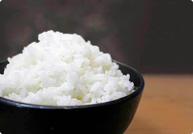 画像：黒いお茶碗にお米が山盛り入っていて、湯気が出ています。